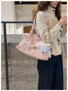 Stilvolle rosa Umhängetasche im koreanischen Stil mit Schnallendetail und Bärenanhänger am Model.