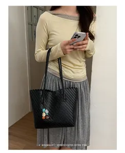 Vista detallada de un bolso tote de cuero tejido negro llevado por una modelo