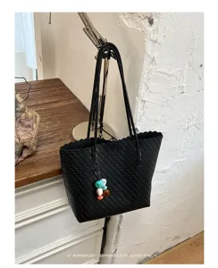 Vista detallada de un bolso tote negro tejido con un colgante de cuentas de colores en un entorno