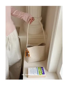 Detail of minimalist cream woven tote bag with wooden bead charm in a French niche style