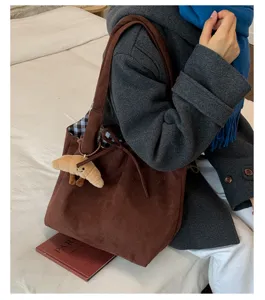 Close-up detail of brown suede tote bag featuring a cute croissant plush charm and plaid lining