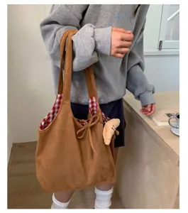 Retro brown suede tote bag with red plaid lining and croissant charm worn by a model