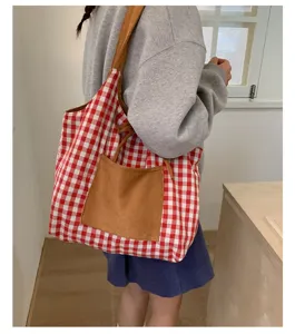 Close-up detail of a red and white gingham tote bag with a brown suede pocket on a model