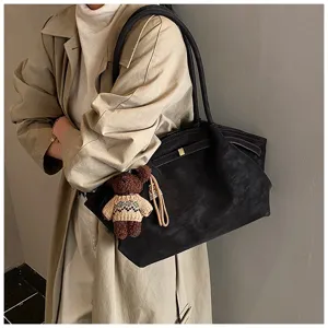 Gros plan d'un grand sac cabas vintage noir avec un charme ours sur un trench