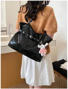 Grand sac cabas noir brillant avec boucle de ceinture et porte-clé chien en peluche sur modèle.