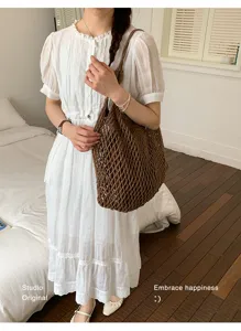 Καφέ πλεκτή τσάντα mesh με λευκό καλοκαιρινό φόρεμα σε φωτεινό εσωτερικό χώρο.