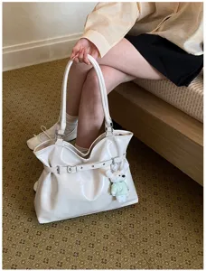 Détail d'un sac cabas crème élégant avec bandoulière et pendentif ours.