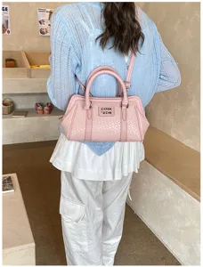 Détail d'un sac à main rose tressé avec logo en métal et texture de la poignée