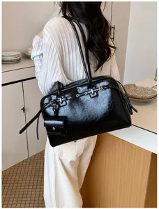 Detailed view of black glossy leather tote bag featuring eyelet straps and small pouch.
