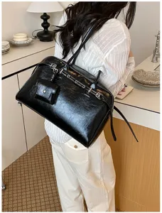 Detail view of a black minimalist soft leather shoulder bag with a mini decorative pouch.