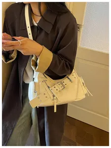 Borsa a spalla bianca crema con borchie e fibbia a cintura indossata da una modella.