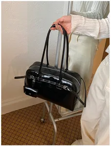 Close-up of black shiny leather shoulder bag with decorative buckles and mini pouch