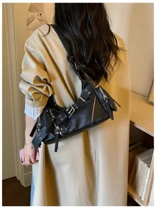 Vista posteriore di una borsa a spalla nera stile moto con borchie e fibbie su un trench beige.
