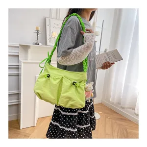 Detail of a lime green utility messenger bag featuring a ruffled strap and bear charm