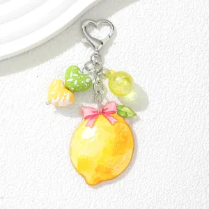 Gros plan d'un porte-clés citron avec des breloques cœur et un nœud rose sur fond blanc