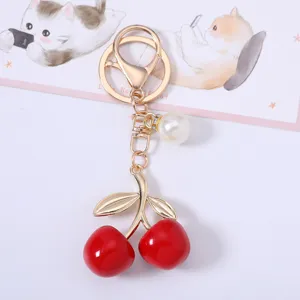 Detailed close-up of a sweet red cherry keychain with golden leaves and white pearl.
