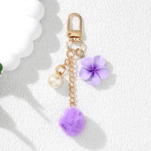 Close-up of a purple resin flower and fluffy pom-pom keychain charm for bag decor