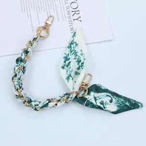 Macro view of woven green silk scarf and gold chain phone strap with metal lobster clasps