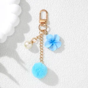 Detailed macro view of blue resin flower and soft pom-pom keychain with gold chain