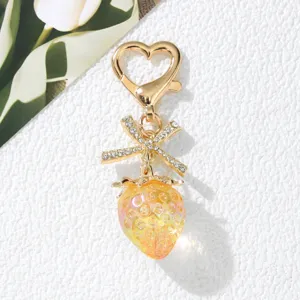 Close-up of a sweet yellow strawberry keychain with rhinestone bow and heart clasp charm
