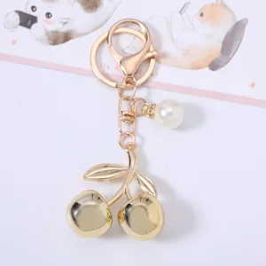 Detailed macro view of a golden cherry keychain featuring an elegant white pearl charm accessory.