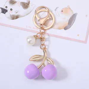 Detailed close-up of a purple cherry keychain with gold metal leaves and pearl charm
