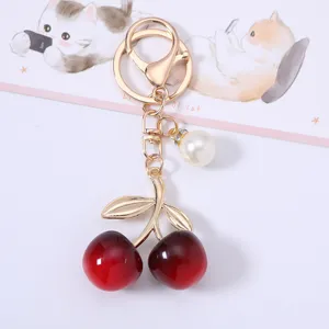 Close-up of a gold metal cherry keychain with red acrylic fruits and a pearl charm