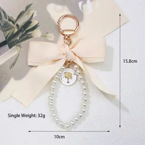 Detailed close-up showing a large beige bow and pearl bead loop keychain for bag accessory