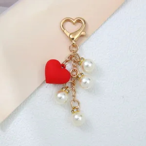 Gros plan d'un porte-clés en forme de cœur avec un charme rouge et des perles blanches