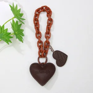 Detalle de un colgante de corazón de cuero marrón con cadena naranja para bolso de moda.