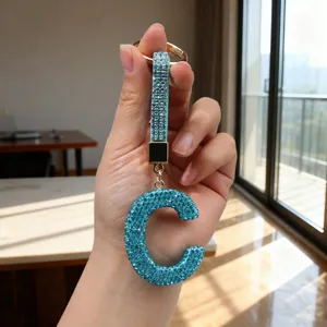 Close-up handheld view of a sparkling blue rhinestone letter C keychain with matching strap