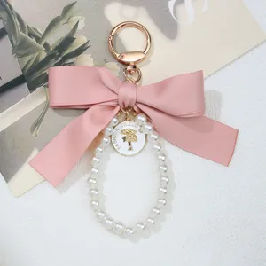Detailed close-up of a pink satin bow and pearl loop keychain with a round gold charm