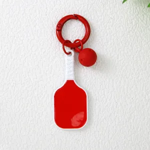 Détail d'un porte-clés raquette de pickleball rouge et blanc avec un petit charme de balle.