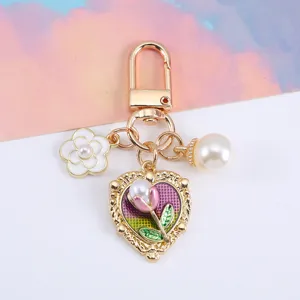 Detailed view of gold heart keychain with pearl and floral charms for bags or AirPods cases.