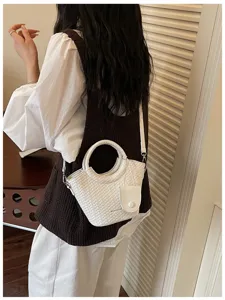 Close-up of white woven bucket bag with circular handle and crossbody strap
