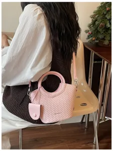 Chic pink bucket bag with embossed woven texture and round top handle worn by a model