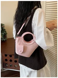 Stylish pink woven texture bucket bag with round handle worn as a casual crossbody bag