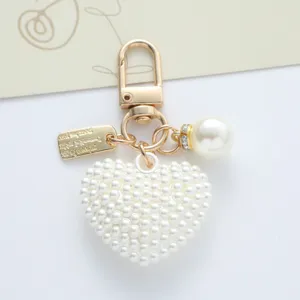 Elegant close-up of a white pearl heart keychain with gold alloy clasp and charms