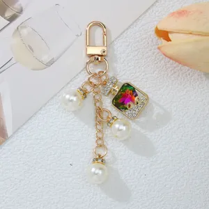 Primer plano del colgante de frasco de perfume y perlas en llavero dorado brillante