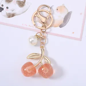 Detailed view of a glittery peach cherry keychain with elegant pearl charm decoration.