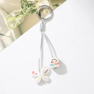 Detailed macro view of cute white butterfly and smile cube charms on silver cord keychain