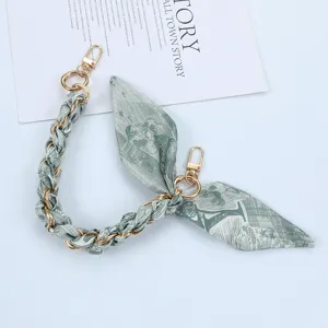 Detailed view of a green patterned silk scarf strap interwoven with a gold metal chain clasp.
