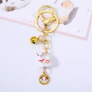 Detail shot of a cute white ceramic cat keychain with a golden bell and charm