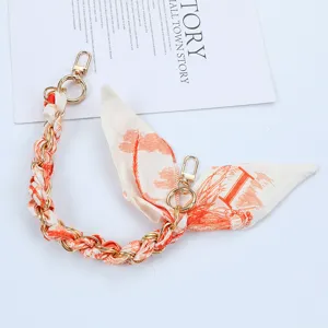 Detailed view of fashion phone strap featuring orange patterned scarf and gold chain