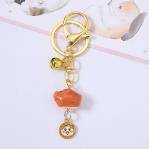 Detail view of a cute ceramic zodiac pig keychain with golden bell and metal ring
