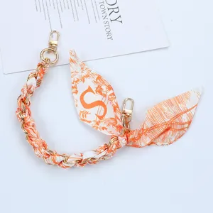 Close-up of orange patterned silk scarf phone strap with letter S and gold clasps