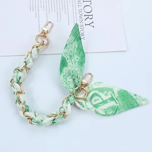 Detail of stylish green silk scarf interwoven with gold metal chain phone strap