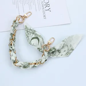 Close-up of golden chain phone strap interwoven with green floral silk scarf