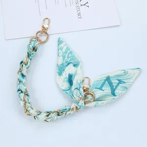 Stylish detail of silk scarf and gold chain phone strap with letter N pattern print