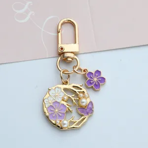 Close-up of gold-tone cherry blossom keychain with purple enamel flower and pearl accents